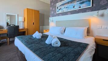 A hotel room with a large bed, a desk, a chair, and a wardrobe.