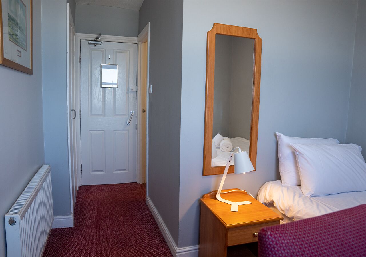 A hotel room with a bed, a bedside table with a lamp, a mirror, and a radiator.