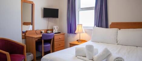 A hotel room with a bed, a desk, a chair, a television, and a window with curtains.