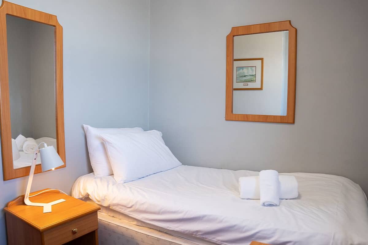 A hotel room with a bed, a bedside table with a lamp, a mirror, and a framed picture on the wall.