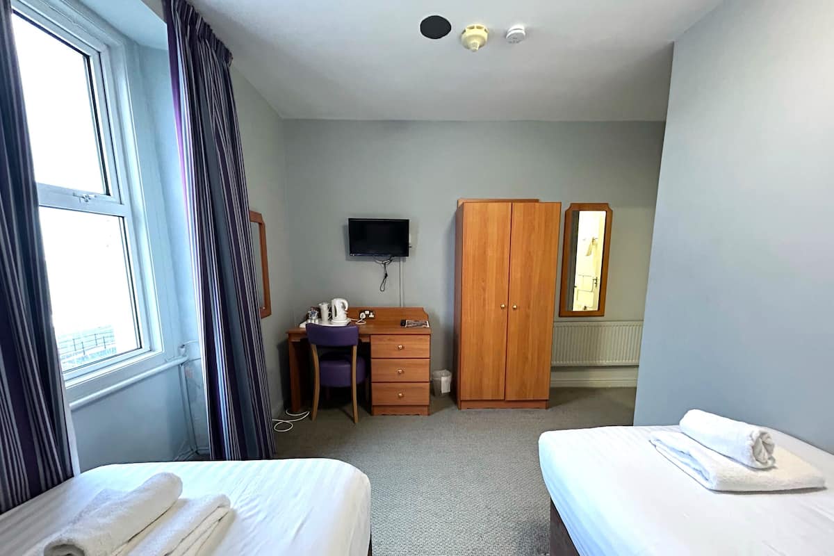 A hotel room with two beds, a desk with a chair, a wardrobe, a television, and a window.