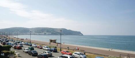 Una carretera costera con coches estacionados, una playa y una caseta de vigilancia.