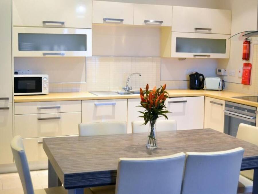 A modern kitchen with white cabinets, a microwave, a toaster, and a sink. There is a dining table with chairs and a vase with flowers.