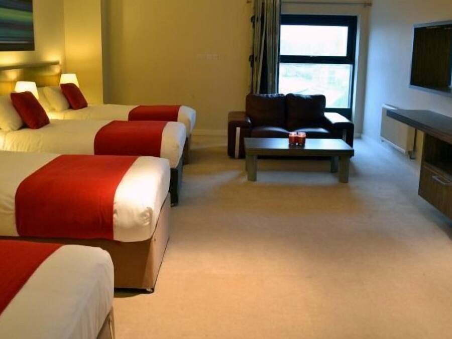 Ein Hotelzimmer mit drei Betten, einer Couch, einem Couchtisch und einem Fernseher.