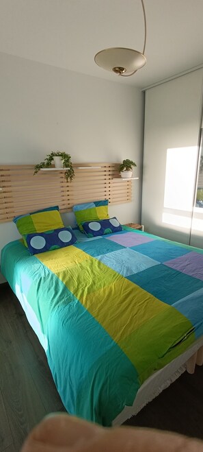 A bed with a colorful quilt, wooden headboard, and two potted plants on shelves.