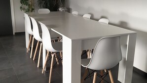 Uma área de jantar moderna com uma mesa branca comprida e seis cadeiras brancas com pés de madeira.