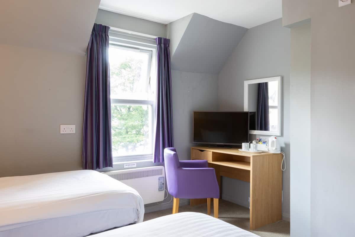 A hotel room with two beds, a desk with a television, and a window with curtains.