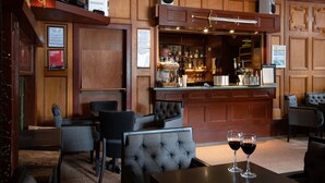 A bar area with wooden paneling, a counter with various bottles, and seating with two glasses of red wine. - Claymore Hotel (Arrochar)