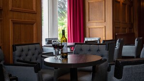 A dining area with a round table, upholstered chairs, and a bottle of wine. - Claymore Hotel (Arrochar)