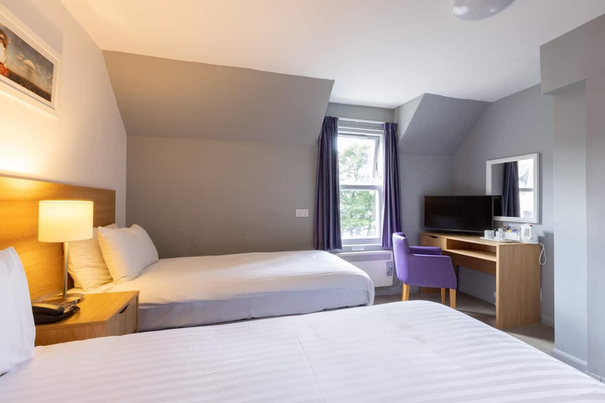 A hotel room with two beds, a desk with a computer, a TV, and a window with curtains.