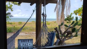 Una hamaca colgada del techo de madera, una ventana con vista a la playa y un letrero con el texto "AMOR & PAZ & M@R".