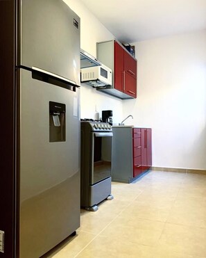 A compact kitchen with a refrigerator, oven, microwave, and red cabinets.
