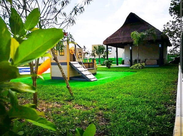 A playground with a slide and a thatched-roof structure.