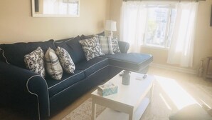 A living room with a dark blue sofa, patterned pillows, a white coffee table, and a window with curtains. - 2 Bd Beach Condo only 2 min walk to OC's Goldcoast (Ocean City)