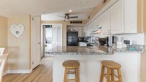 A modern kitchen with white cabinets, granite countertops, and a central island with stools. - 2 Bd Beach Condo only 2 min walk to OC's Goldcoast (Ocean City)