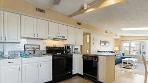 A modern kitchen with white cabinets, a black stove, and a dishwasher. There is a coffee maker on the counter and a welcome sign above the stove. - 2 Bd Beach Condo only 2 min walk to OC's Goldcoast (Ocean City)