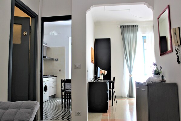 A modern kitchen with a washing machine, a dining area with a black table and chairs, and a small cabinet with a mirror and phone.