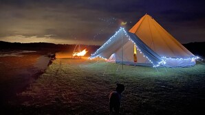 Une grande tente illuminée, avec un feu qui brûle à l’arrière-plan.