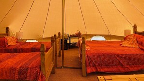 Une tente avec deux lits, chacun doté d’un cadre en bois et de draps rouges. Une table avec une lampe et une bouilloire se trouve entre les deux lits.