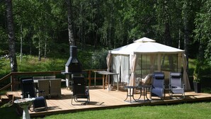 Eine Holzterrasse mit Gartenmöbeln, einem Zelt und einem Grill.