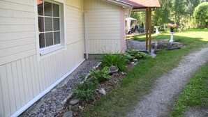 Ein Haus mit überdachter Veranda, einem Fenster und einem Garten mit Pflanzen und einem Vogelbad.