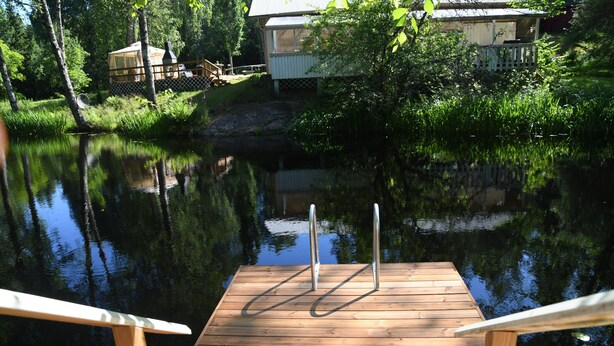 Eine Holzsteg, der sich in ruhiges Wasser erstreckt, mit einem Haus im Hintergrund.