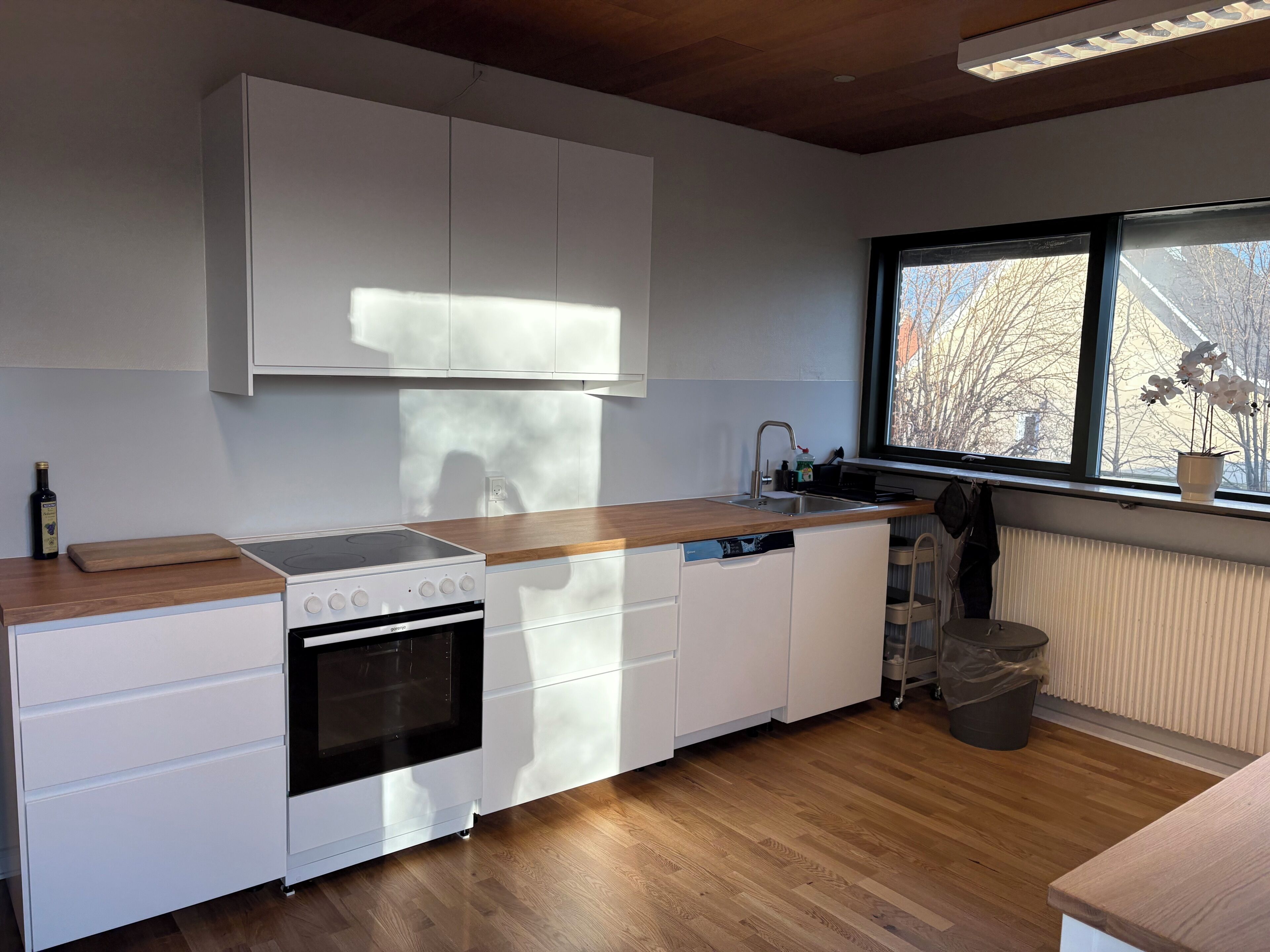 Een moderne keuken met witte kasten, een houten aanrecht, een ingebouwde oven en een raam met uitzicht op bomen.