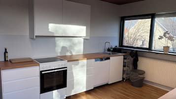 Una cocina moderna con armarios blancos, encimera de madera, horno empotrado y ventana con vistas a árboles.