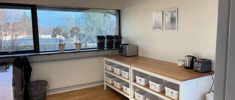 Een keuken met houten kastjes, een raam met plantenpotten, een waterkoker en een broodrooster.