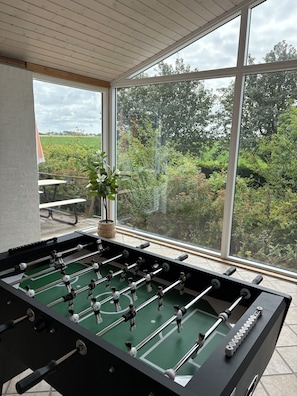 A foosball table in a room with large windows overlooking a garden.