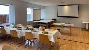 Un salón de conferencias con mesas dispuestas para una comida, una pantalla de proyector y un ventanal grande.