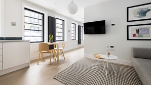 Ein modernes Wohnzimmer mit Flachbildfernseher, einem grauen Sofa und einem Essbereich mit Holzkstühlen und einem kleinen Tisch.