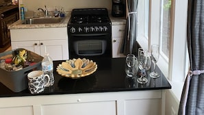 A compact kitchen with white cabinets, a black stove, a microwave, and a window with curtains. - Little Piece of Heaven in the North Georgia Mountains (Dahlonega)