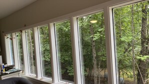 A room with large windows offering a view of a forest. There is a laptop on a table, a bowl, and a butterfly decoration on the windowsill. - Little Piece of Heaven in the North Georgia Mountains (Dahlonega)