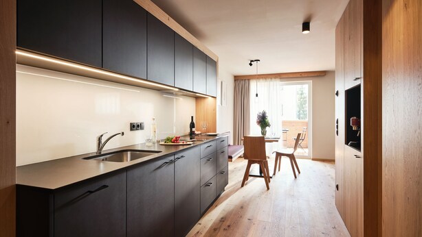A modern kitchen with dark cabinets, a wooden countertop, and a dining area with a table and chairs. - Apartments Alpe di Susi - Holiday Apartments in the Italian Dolomites (Castelrotto)