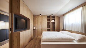 A modern bedroom with a wooden wardrobe, built-in TV, and a large bed with white bedding. - Apartments Alpe di Susi - Holiday Apartments in the Italian Dolomites (Castelrotto)