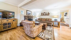 Un salón amplio con suelo de madera, un sillón de cuero, un conjunto de sofás, un televisor y una chimenea de piedra.