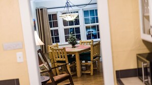 Un comedor con una mesa y sillas de madera, una lámpara colgante y un ventanal con cortinas.