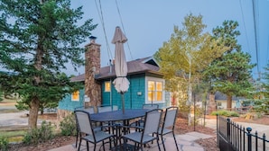 Un patio con una mesa y sillas, una chimenea de piedra y una casa con fachada azul.