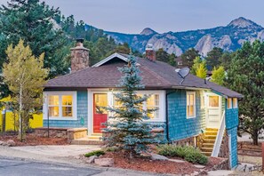 Une maison de plain-pied avec une cheminée, un petit porche et une vue sur les montagnes en arrière-plan.