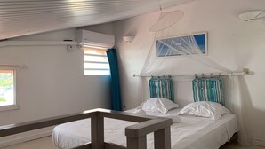 Ein Schlafzimmer mit Bett, Fenster, Deckenventilator und Moskitonetz.