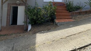 Ein zweistöckiges Gebäude mit grauer Fassade, weißen Fensterläden und einer kleinen Veranda.