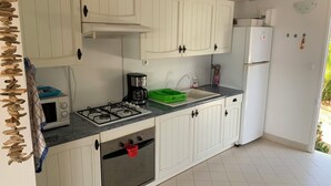 Eine Küche mit weißen Schränken, einem Gasherd, einer Kaffeemaschine, einer Spüle und einem Kühlschrank.