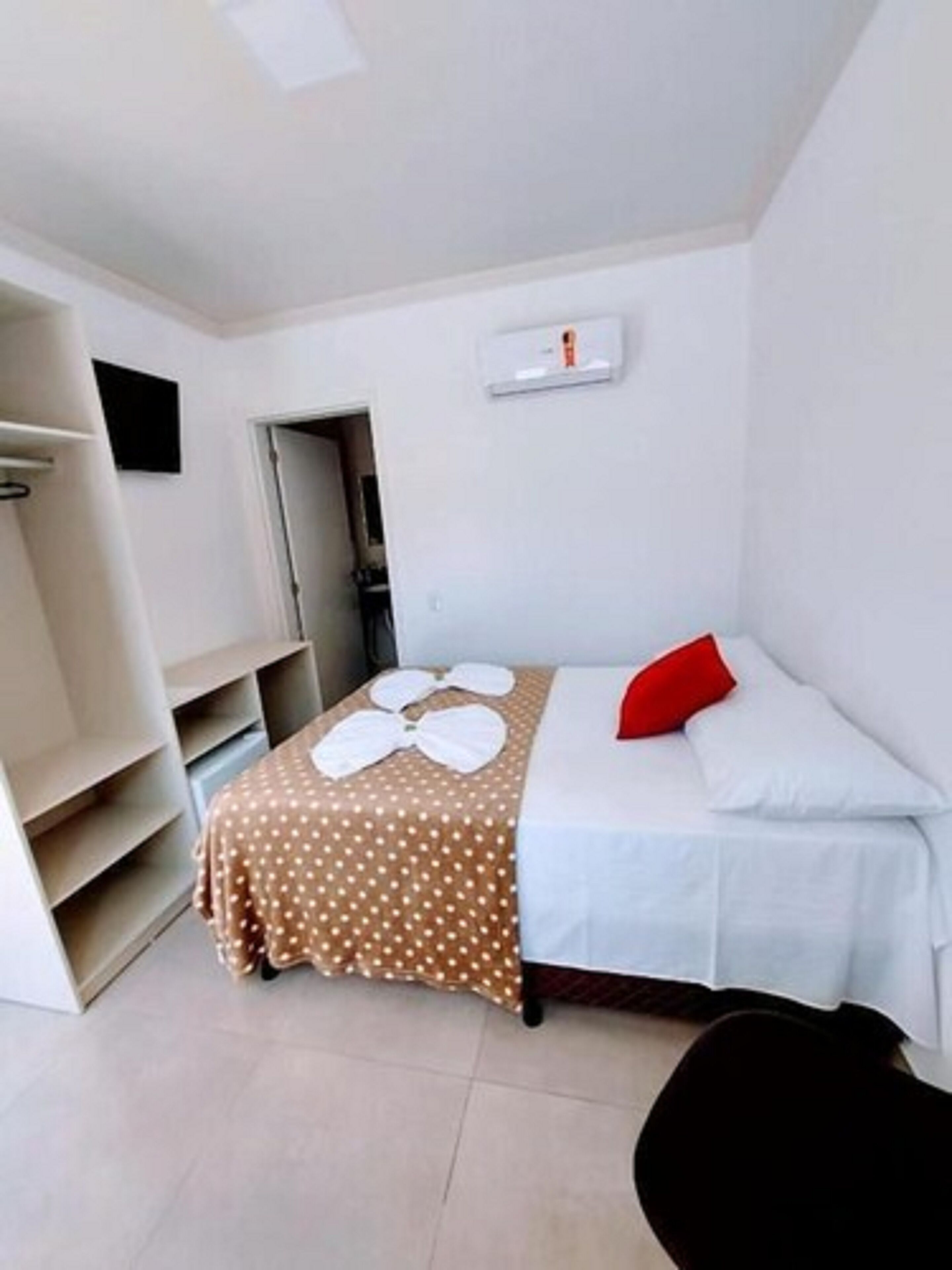 Una camera da letto piccola e ordinata con un letto, un cuscino rosso e un termosifone bianco a parete.