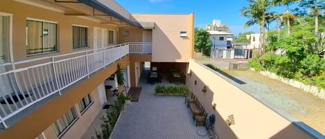 Un edificio de varios niveles con balcones, un patio empedrado y zonas verdes circundantes.