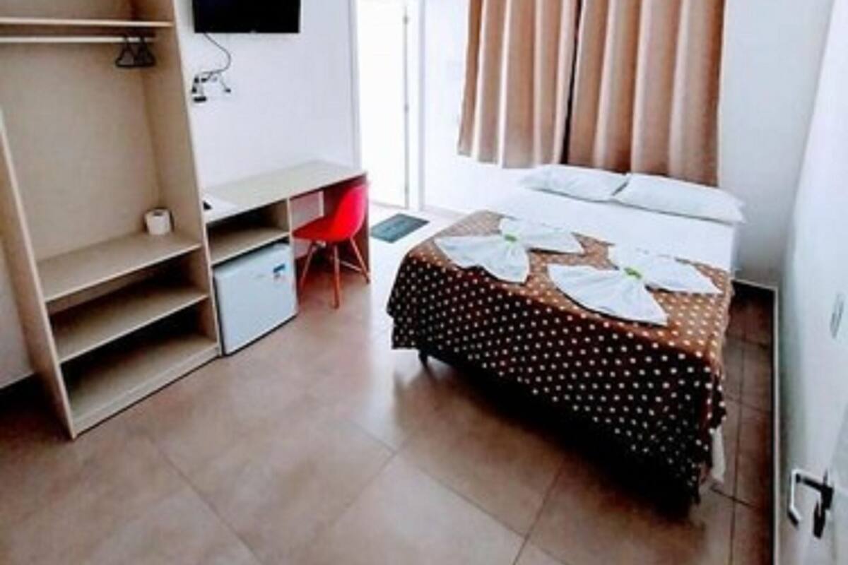 A hotel room with a bed, a desk, a chair, and a TV mounted on the wall.