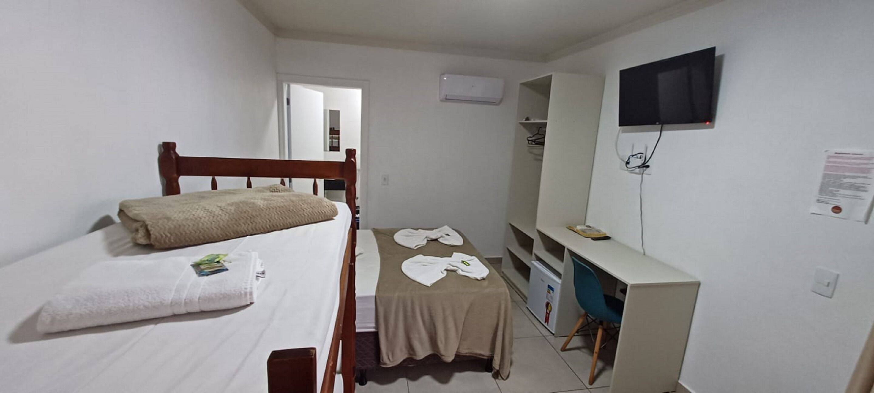Una habitación pequeña y limpia con una cama individual, un escritorio, una silla, un televisor y un armario.