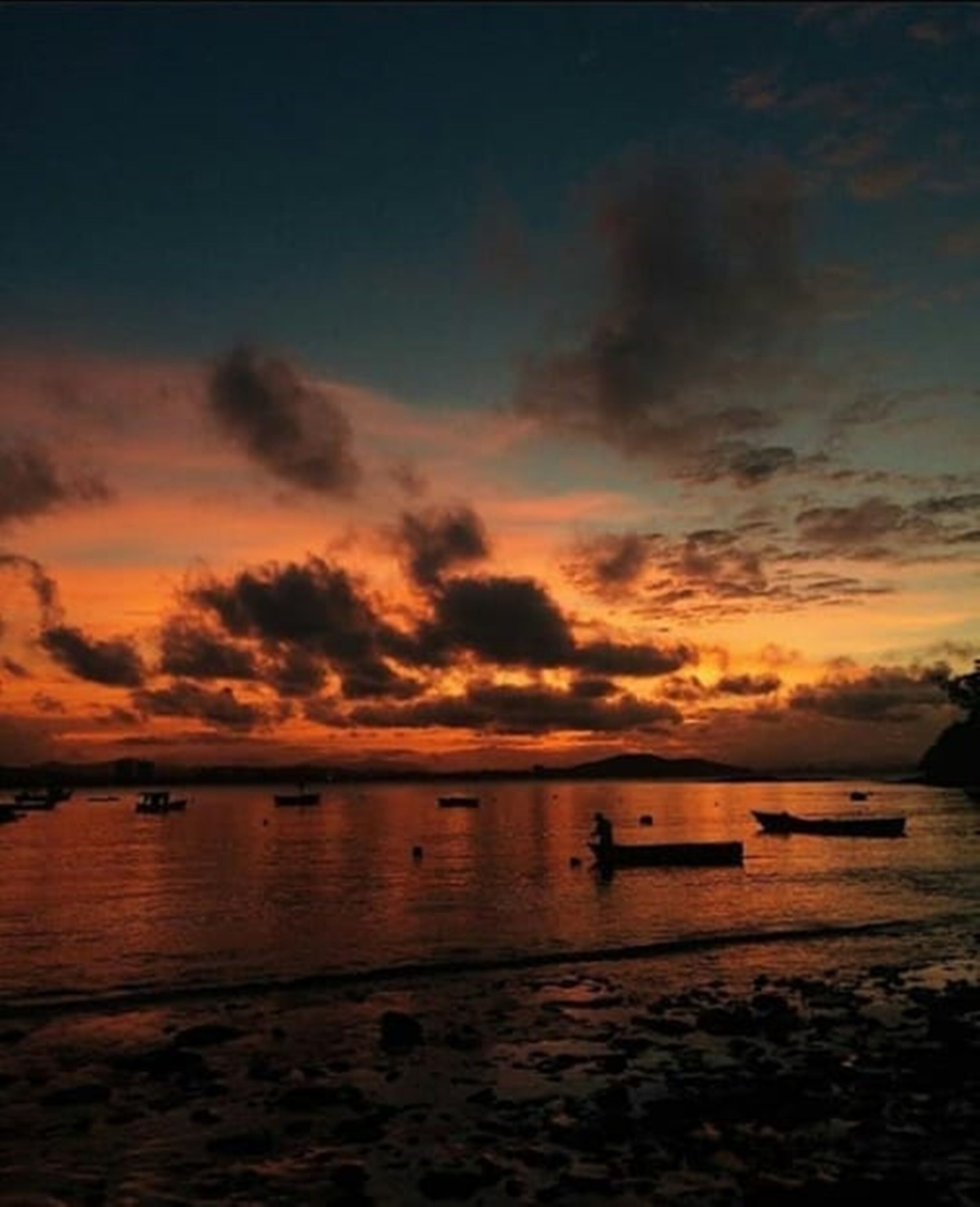 A sunset over a calm body of water with boats.