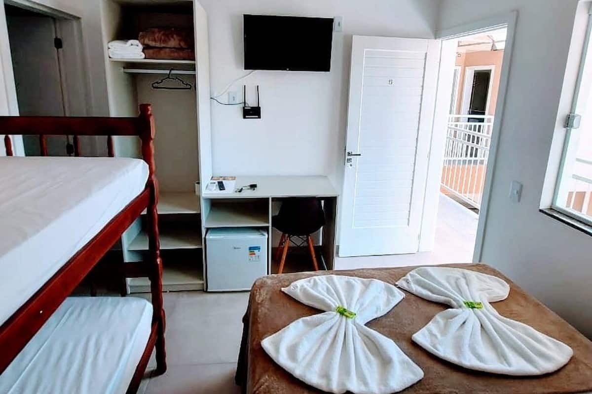 A room with a bunk bed, a desk with a computer, a TV, and a door leading to an outdoor balcony.