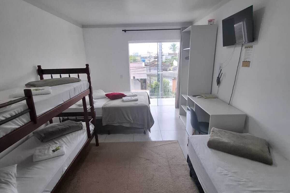 A dormitory room with bunk beds, a desk, a television, and a window with a view of buildings.